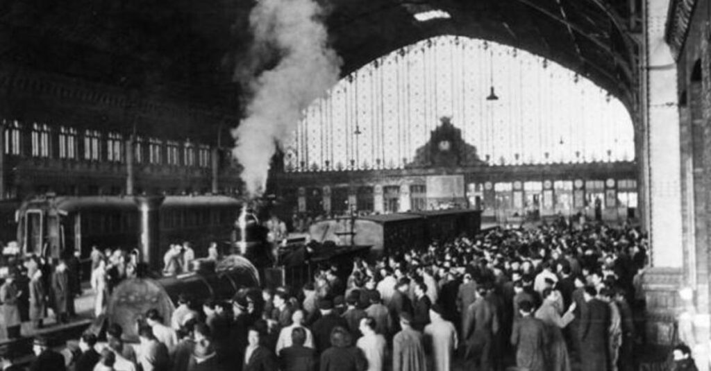 Estación de Atocha antigua con tren de vapor y multitud de pasajeros bajo la marquesina histórica en Madrid