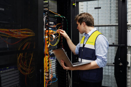 Técnico de Tecmelec trabajando en un armario de telecomunicaciones con cables de fibra óptica y equipos de conexión.